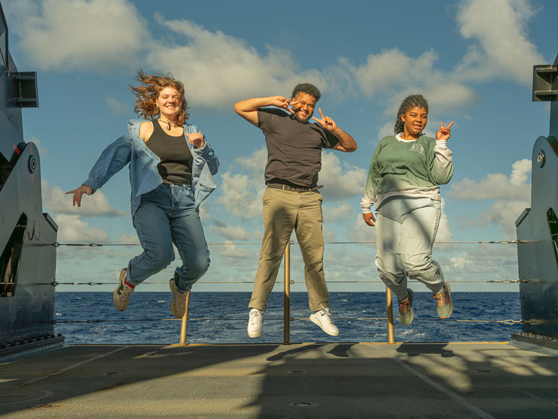 Explorers-in-Training (from left to right) Abby Norstad, Nathanael Mathis, and Gina Knox jump for joy on the back deck of NOAA Ship Okeanos Explorer, demonstrating their enthusiasm for their at-sea experience with NOAA Ocean Exploration.