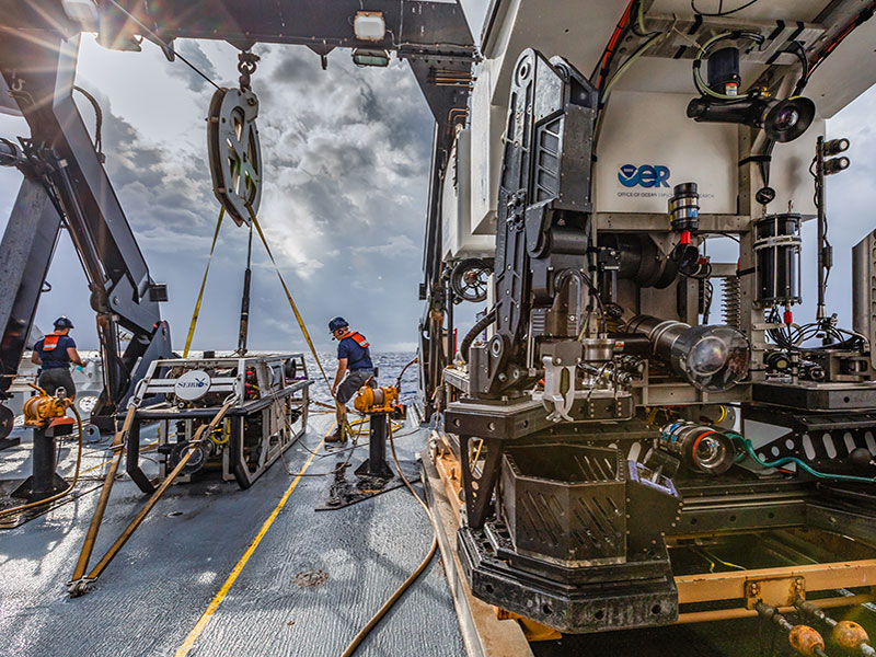 People on a ship's deck deploying a remotely operated vehicle into the ocean.